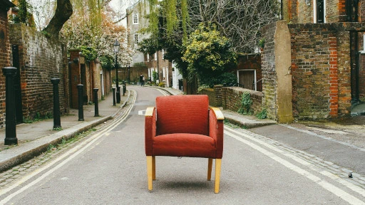 a red chair placed directly in the middle of a street lined with brick houses