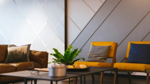 two yellow chairs with a single pillow each alongside a lather couch